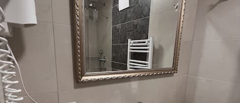 Un baño con un lavamanos blanco, un espejo con marco decorativo, un perchero y un secador de pelo en la encimera.