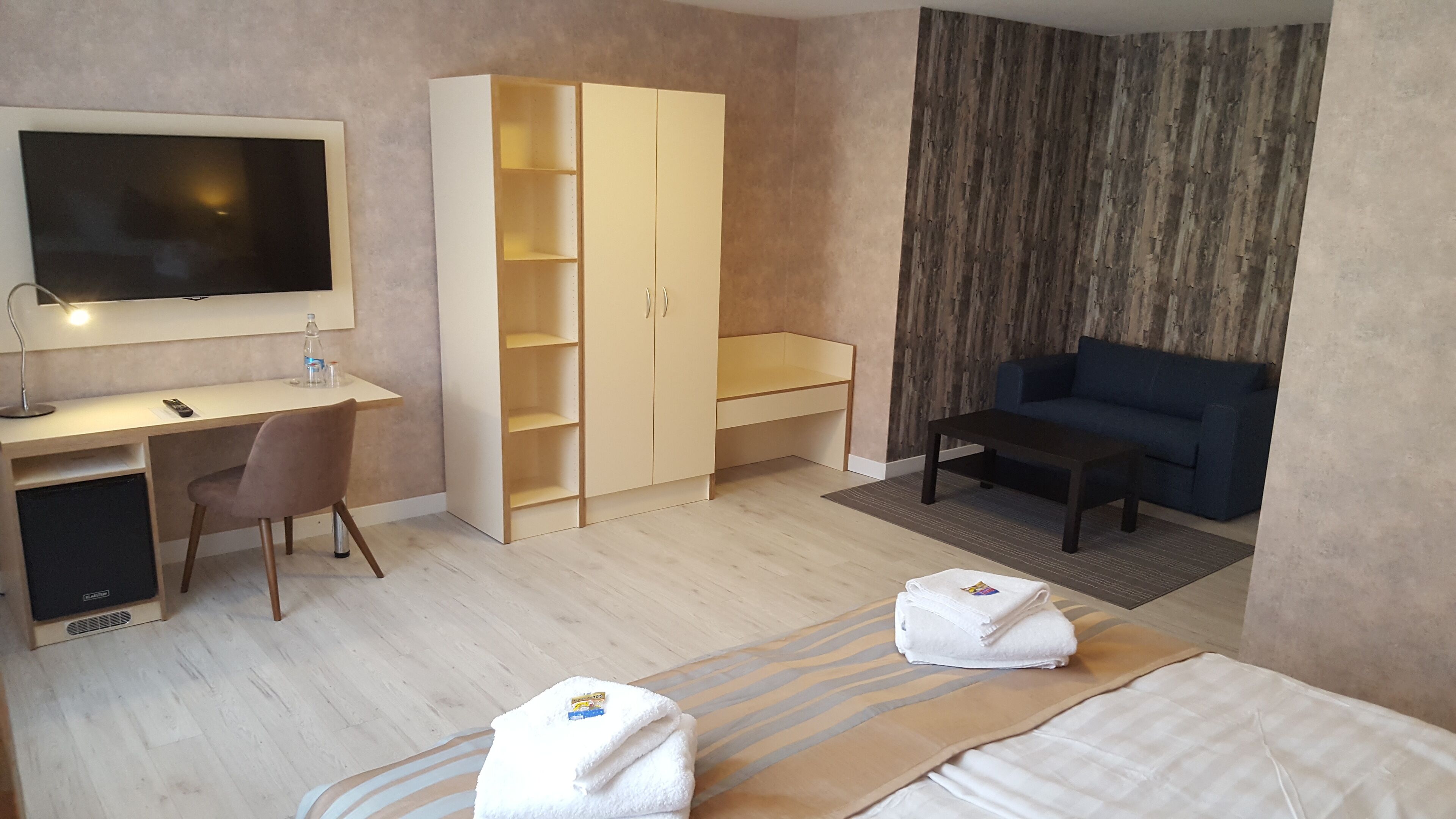 A hotel room with a desk, chair, wardrobe, sofa, and two beds.
