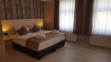 Habitación de hotel moderna con una cama grande, una mesita de noche, una lámpara y vistas al exterior a través de cortinas translúcidas.
