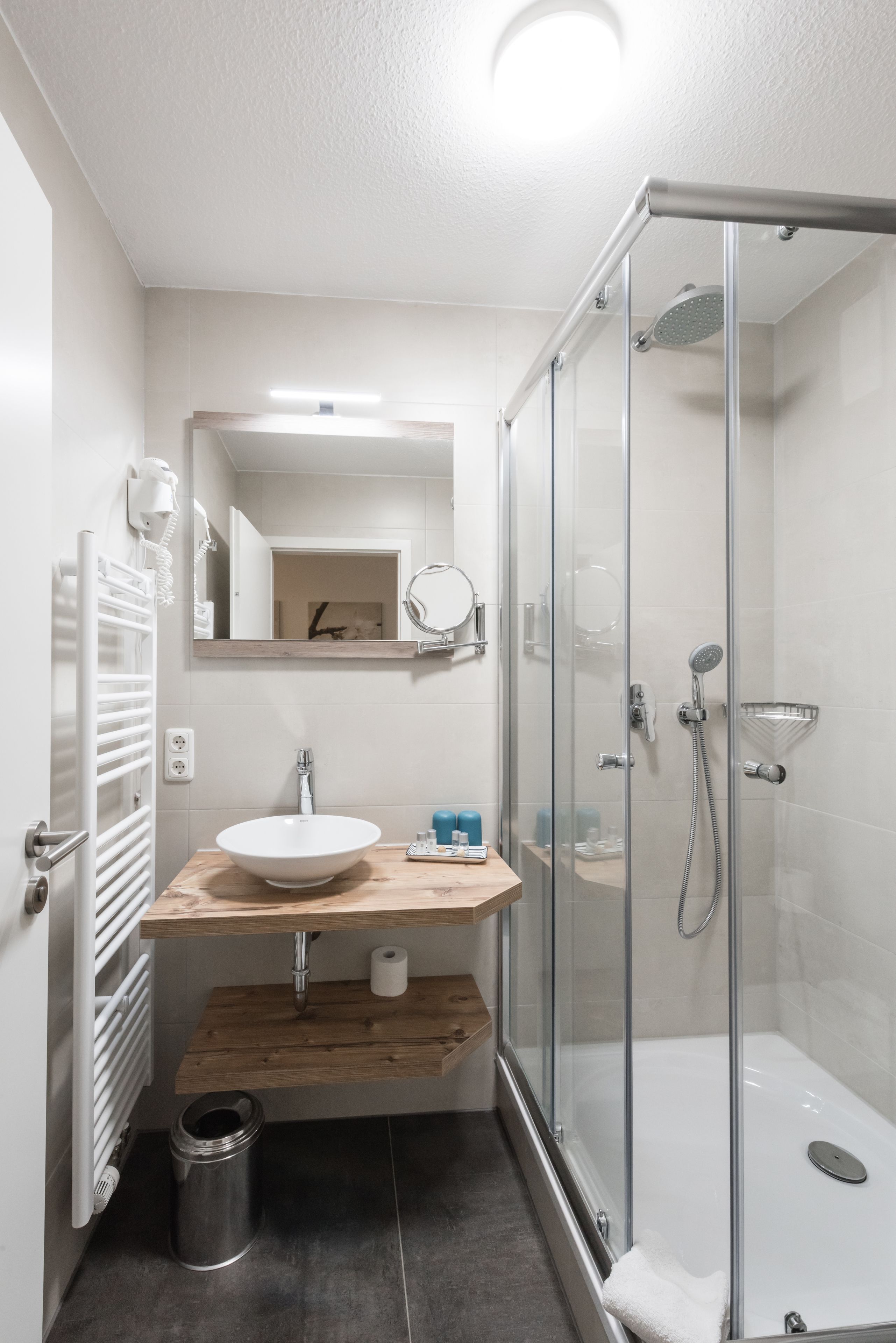 Un baño moderno con ducha de vidrio, tocador de madera, lavabo blanco y espejo sobre el tocador.