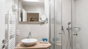 Un baño moderno con ducha de vidrio, tocador de madera, lavabo blanco y espejo sobre el tocador.