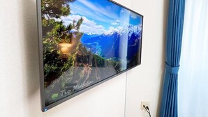 Televisão de tela plana fixada na parede exibindo uma paisagem montanhosa.