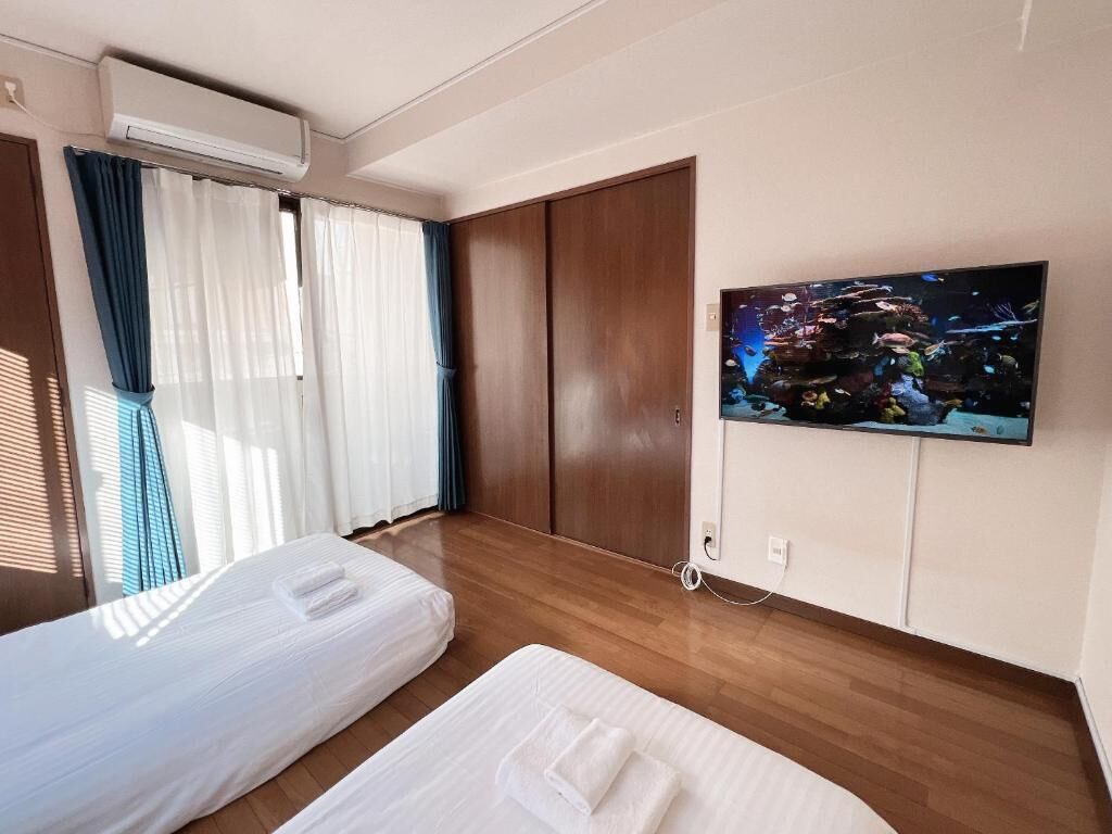 Una camera d'albergo con due letti, una televisione a parete e un'ampia finestra con tende.