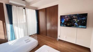 Una camera d'albergo con due letti, una televisione a parete e un'ampia finestra con tende.