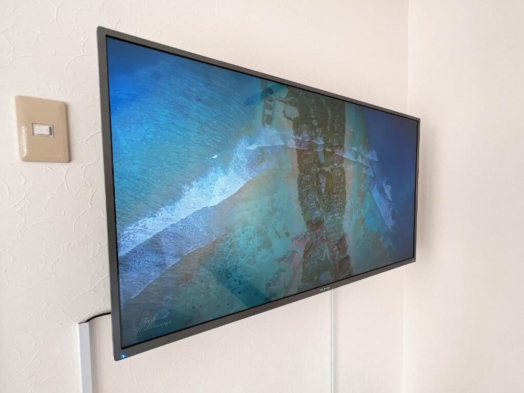 A flat-screen TV mounted on a wall displaying a tropical beach scene.