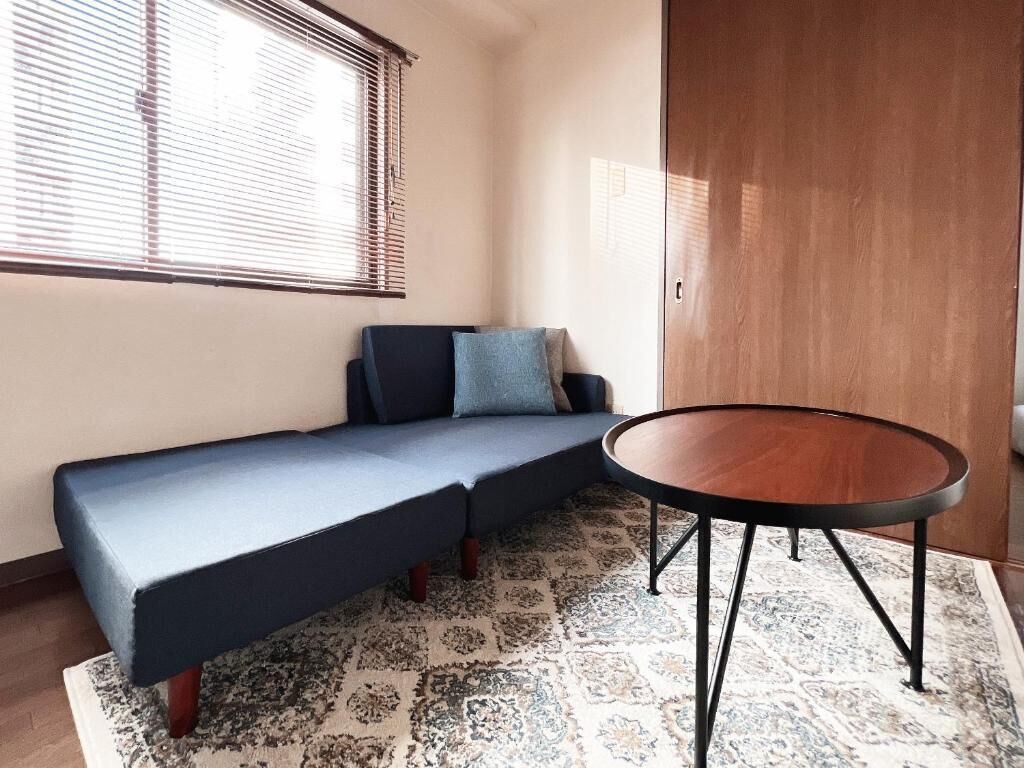 Une pièce avec un canapé bleu, une table ronde en bois et un tapis à motifs.