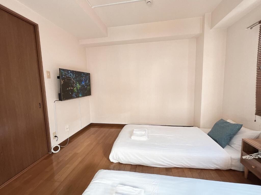 Una habitación con dos camas, un televisor montado en la pared y piso de madera.