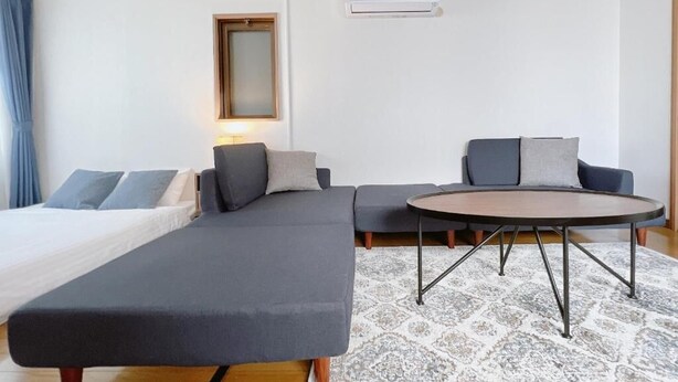 Quarto de hotel moderno com uma cama de solteiro, um sofá, uma mesa de centro redonda e um tapete estampado.