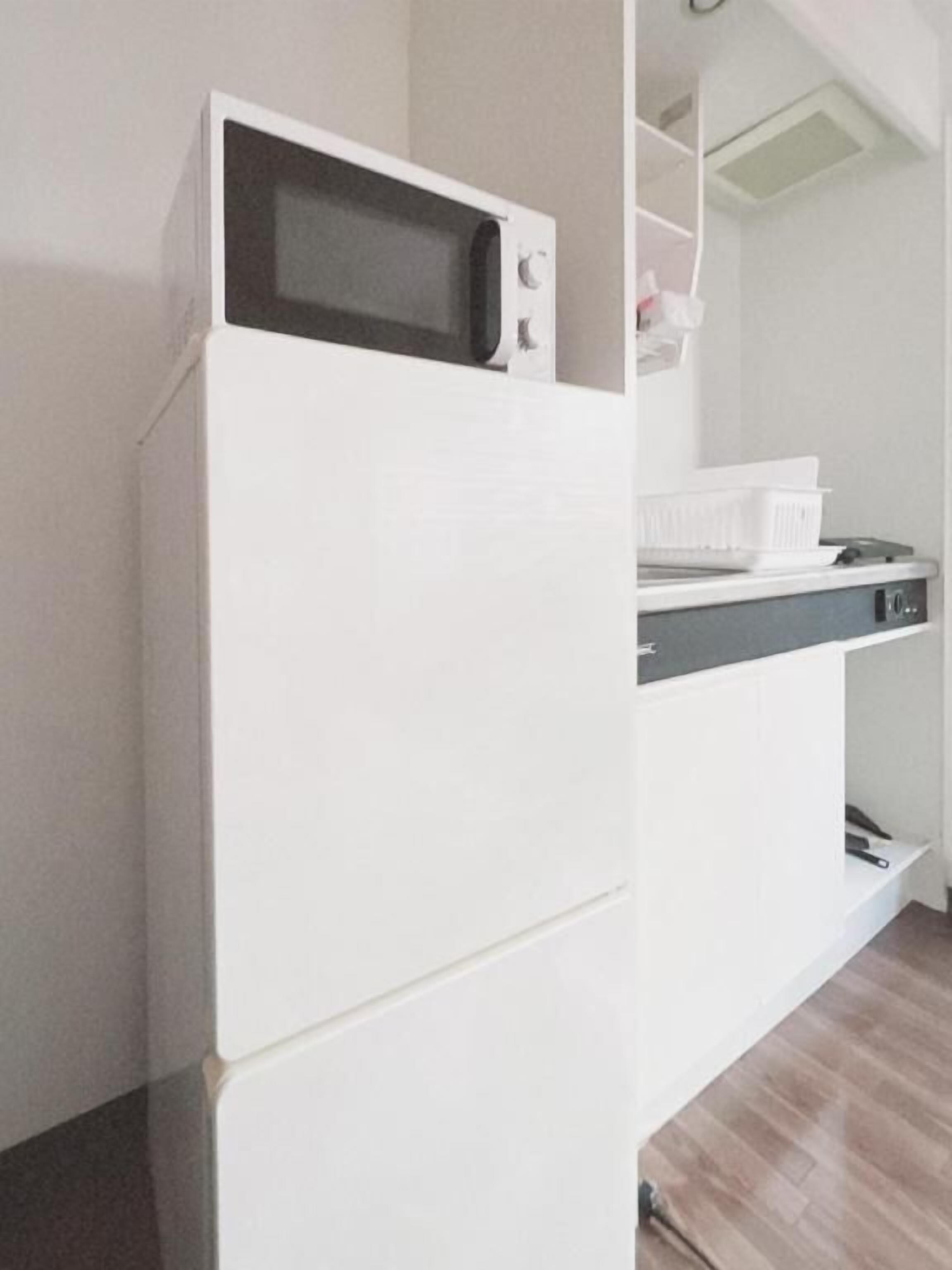 Une cuisine équipée d’un four à micro-ondes, d’un réfrigérateur blanc et d’un plan de travail sur lequel se trouvent un égouttoir et un petit appareil électroménager.