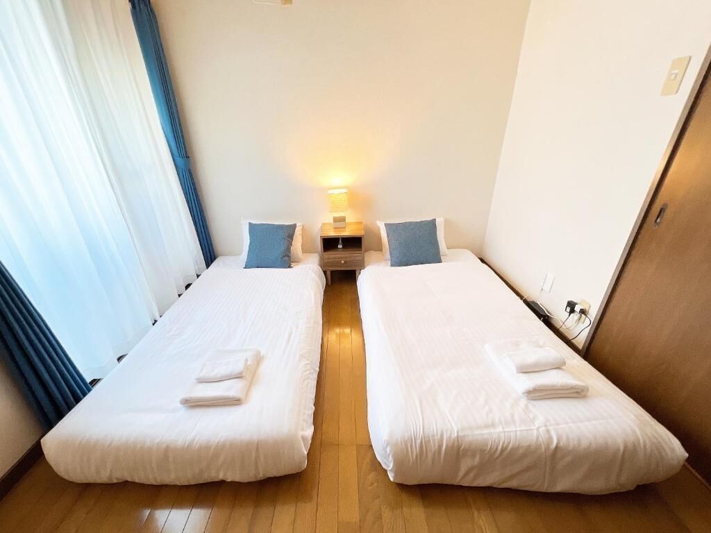A hotel room with two single beds, a nightstand with a lamp, and a wooden floor.