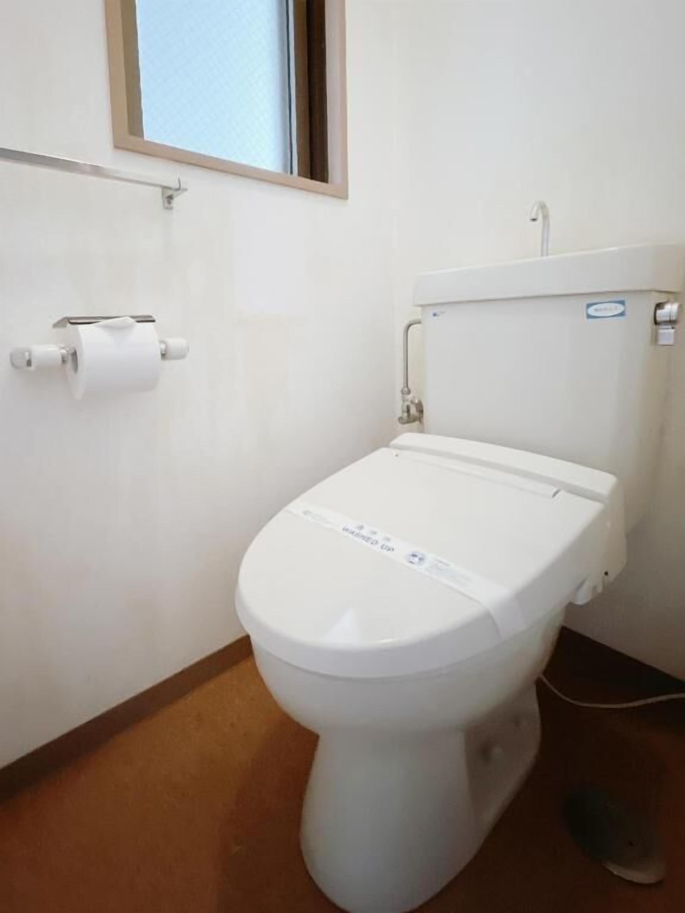 A white toilet with a flush handle and a paper towel holder on the wall.