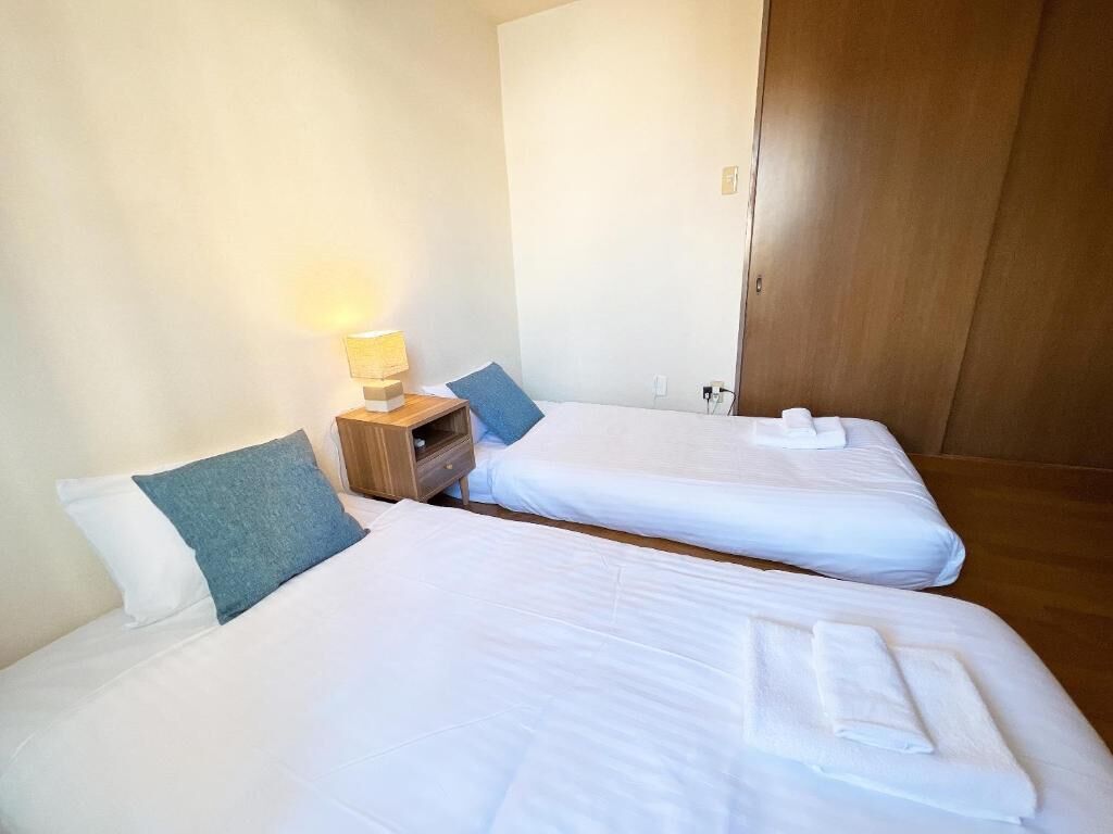 A hotel room with two single beds, a bedside table with a lamp, and a wooden wardrobe.