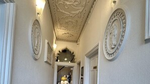 A hallway with ornate ceiling decorations, white walls, and a wooden floor. - Watermead House (Chard)