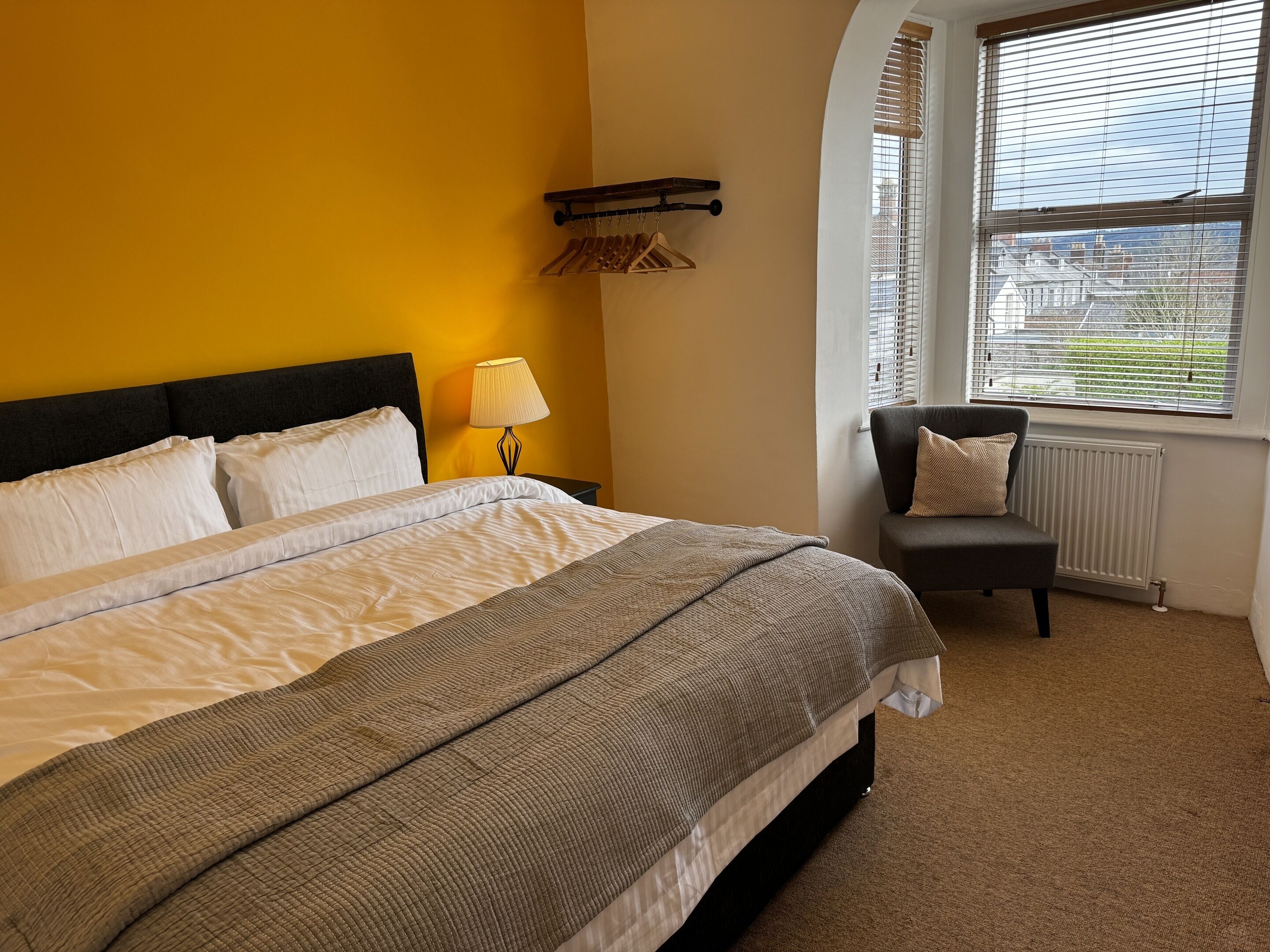 Ein Hotelzimmer mit Bett, Sessel, Lampe und einem Fenster mit Jalousien.