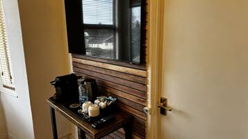 Hotelkamer met een wand van houten panelen, een klein tafeltje met een koffiezetapparaat, bekers en een afstandsbediening.