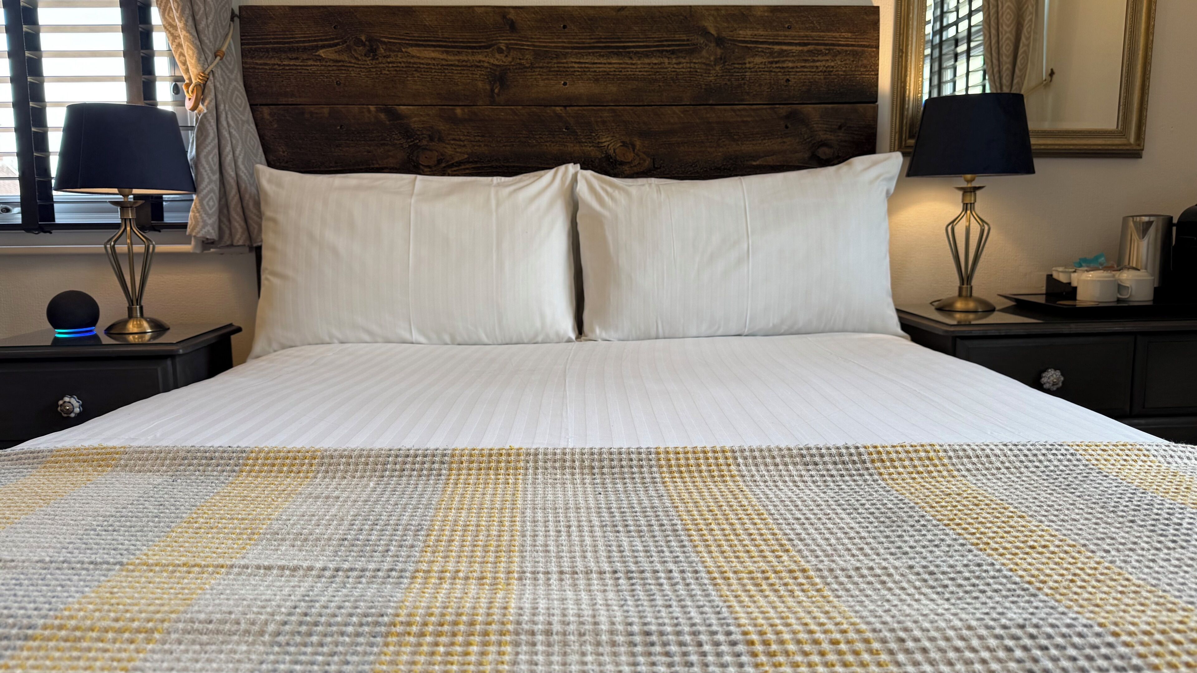 Una cama bien hecha con sábanas blancas, dos lámparas de noche y un cabecero de madera.
