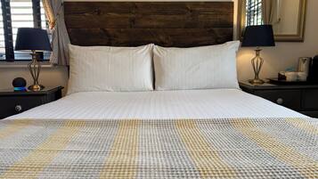 Una cama bien hecha con sábanas blancas, dos lámparas de noche y un cabecero de madera.