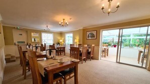 A dining area with wooden tables and chairs, a chandelier, and a view through large sliding glass doors. - Watermead House (Chard)
