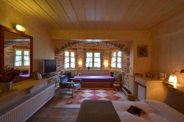 Una habitación acogedora con un arco de piedra, una cama, un escritorio, una silla, un televisor y una ventana con vistas al exterior.