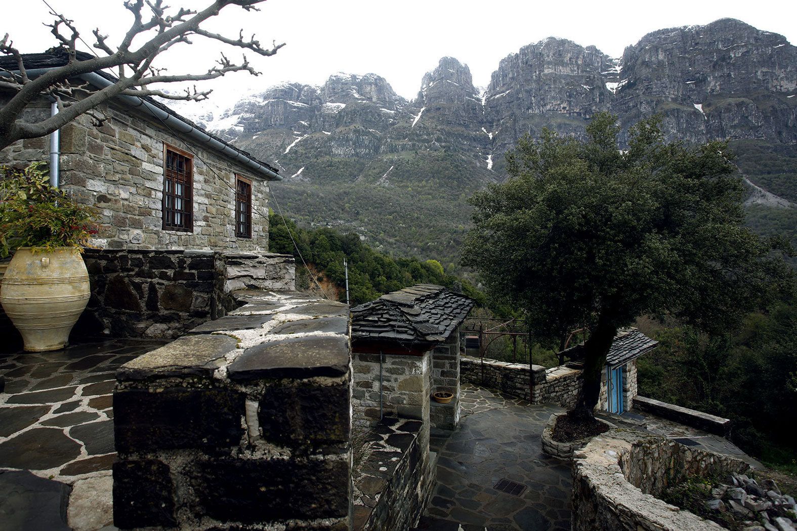 A stone building with a window and a door, surrounded by a stone pathway and a tree.