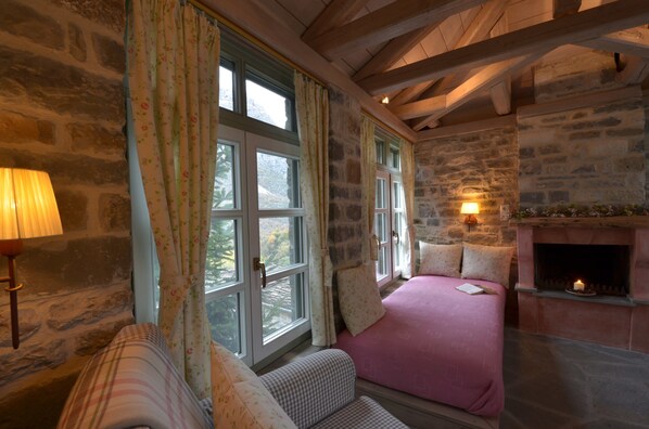 Una habitación acogedora con chimenea de piedra, una cama con ropa de cama rosa y una ventana con cortinas estampadas.