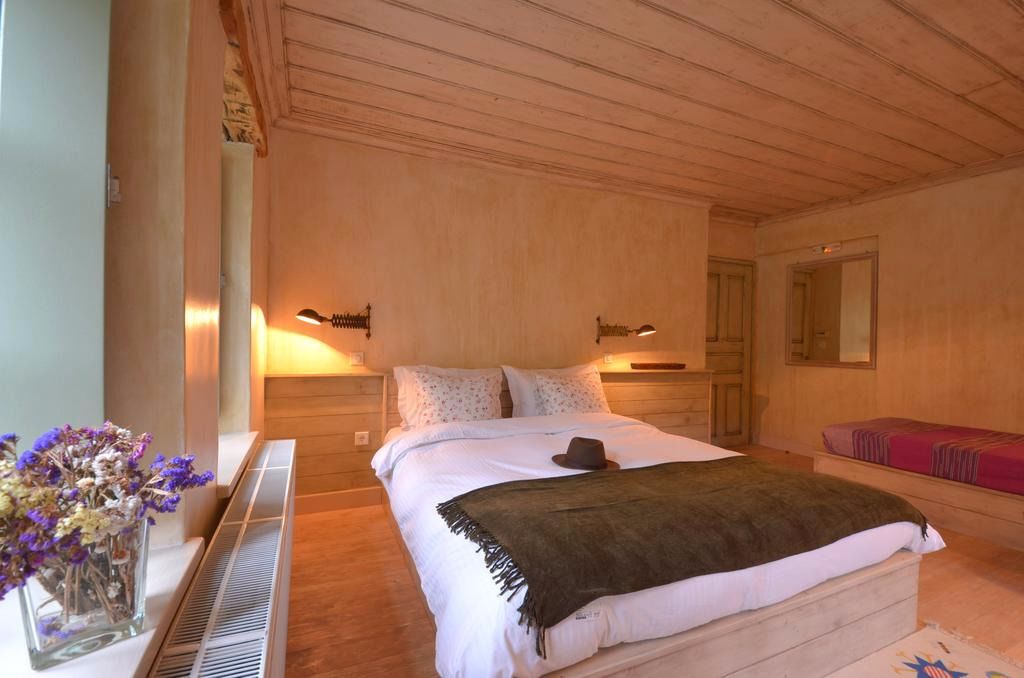 Une chambre à coucher avec un grand lit, des lampes de chevet, une petite table ornée d’un vase de fleurs et un banc avec une couverture.