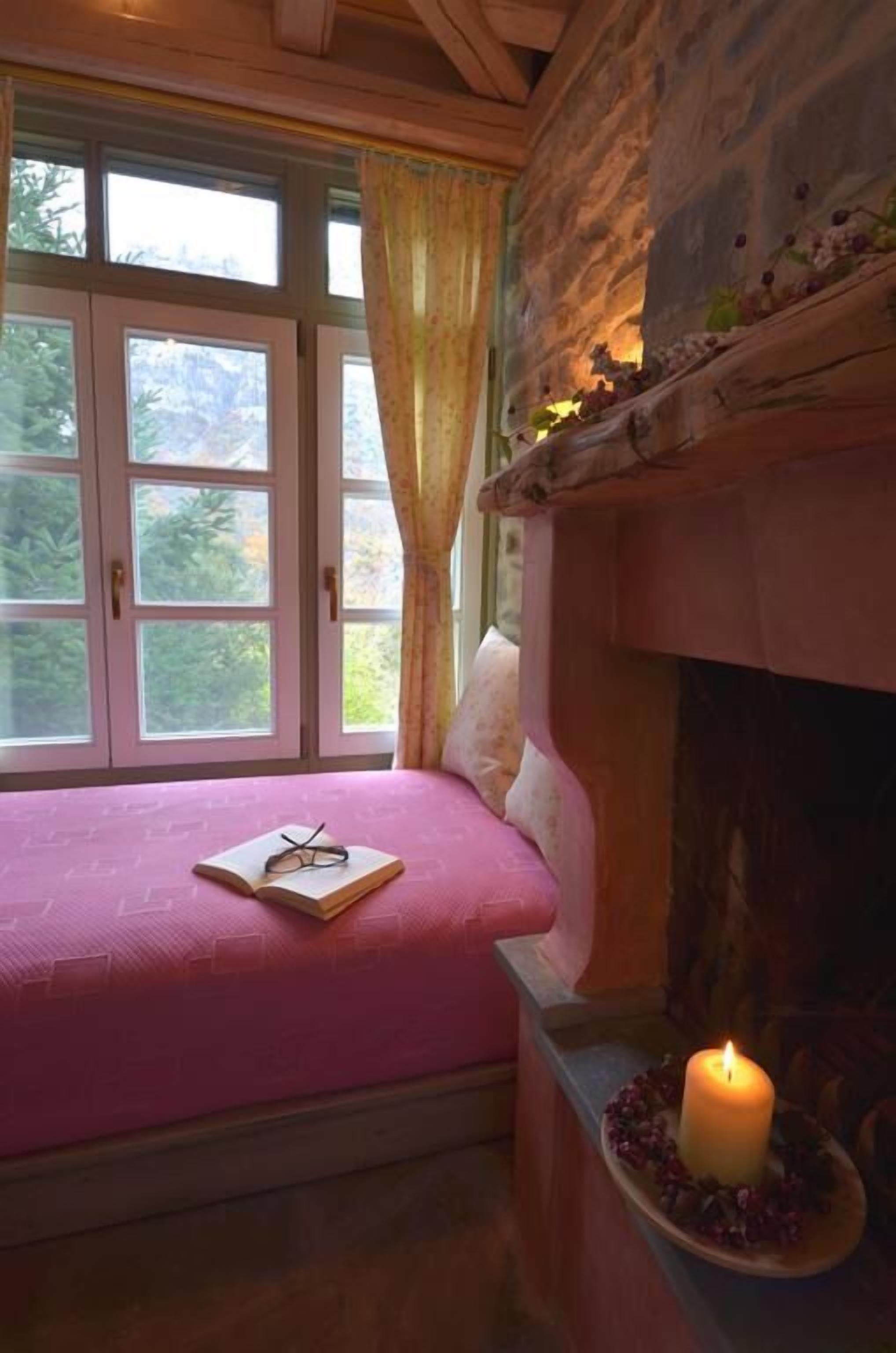 Un dormitorio con chimenea de piedra, colcha rosa y una vela encendida sobre una bandeja.