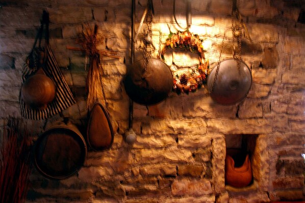 Pared de piedra rústica con diversos utensilios y utensilios de cocina colgados.