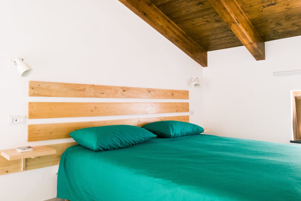 A bedroom with a wooden headboard, a green bedspread, and a white wall.