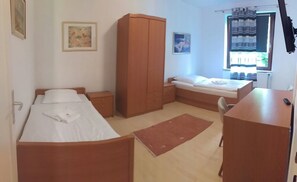 A small, tidy room with two single beds, a wooden wardrobe, a desk, and a chair. - Pension Donau Apartments (Hannover)