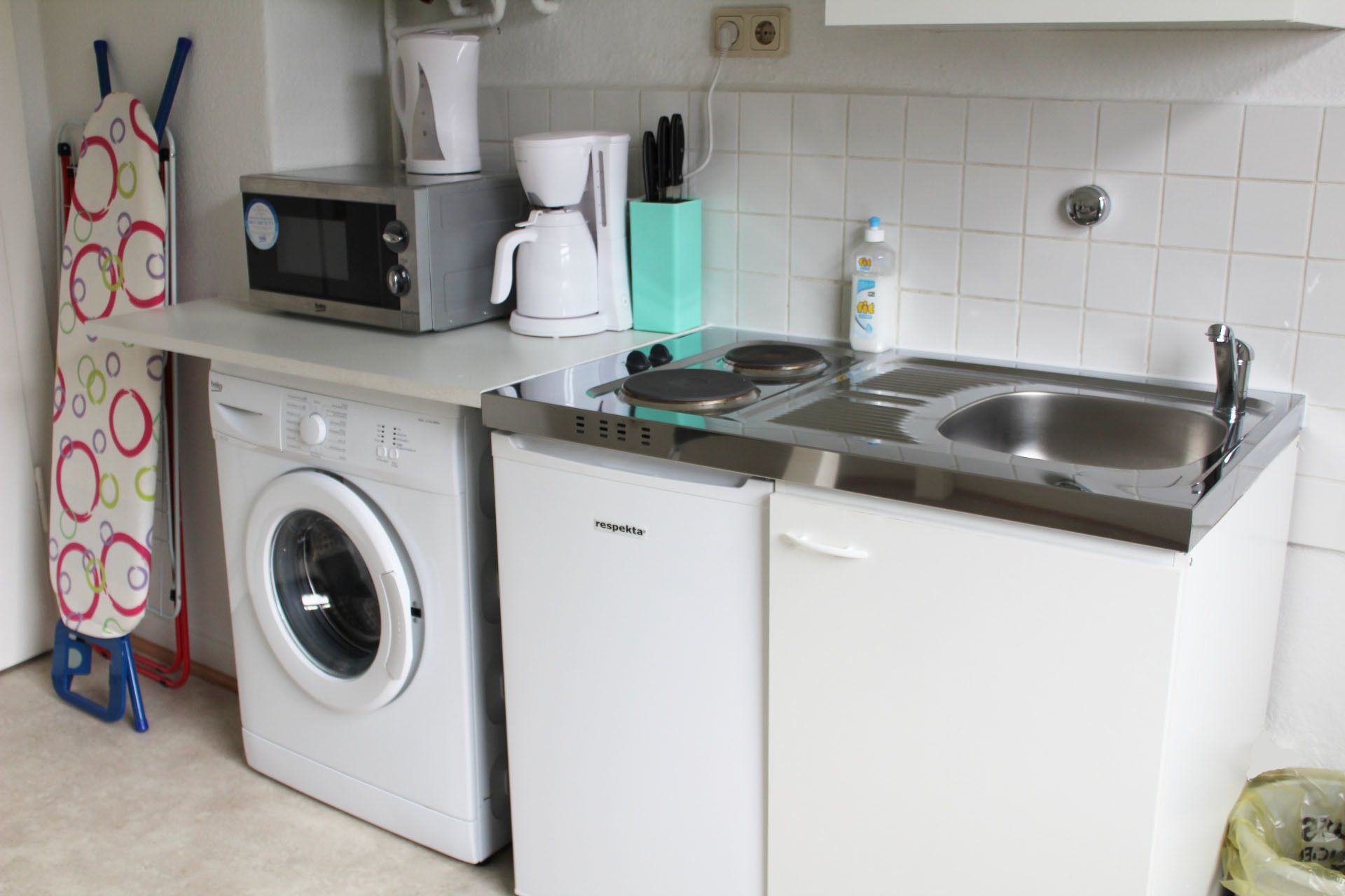 A compact kitchen with a washing machine, a microwave, a coffee maker, and a sink.