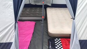 Une tente avec deux matelas de couchage, un rose et un beige, et un sac à carreaux.