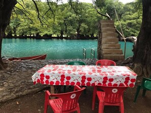 A table with a red and white apple pattern tablecloth, surrounded by red chairs, set against a backdrop of a turquoise lake and green trees. - Anaya & Rodriguez Shop - Hostel (Tangancicuaro de Arista)