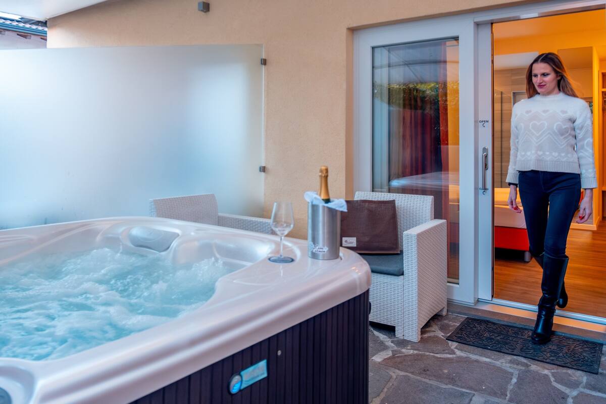 A hot tub with a bottle of champagne, wicker furniture, and a glass of wine.