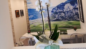 Ein Empfangsschalter mit einer Berglandschaftsmalerei, eine mit Orchidee bepflanzte, grün gemusterte Vase und ein gerahmtes Bild an der Wand.