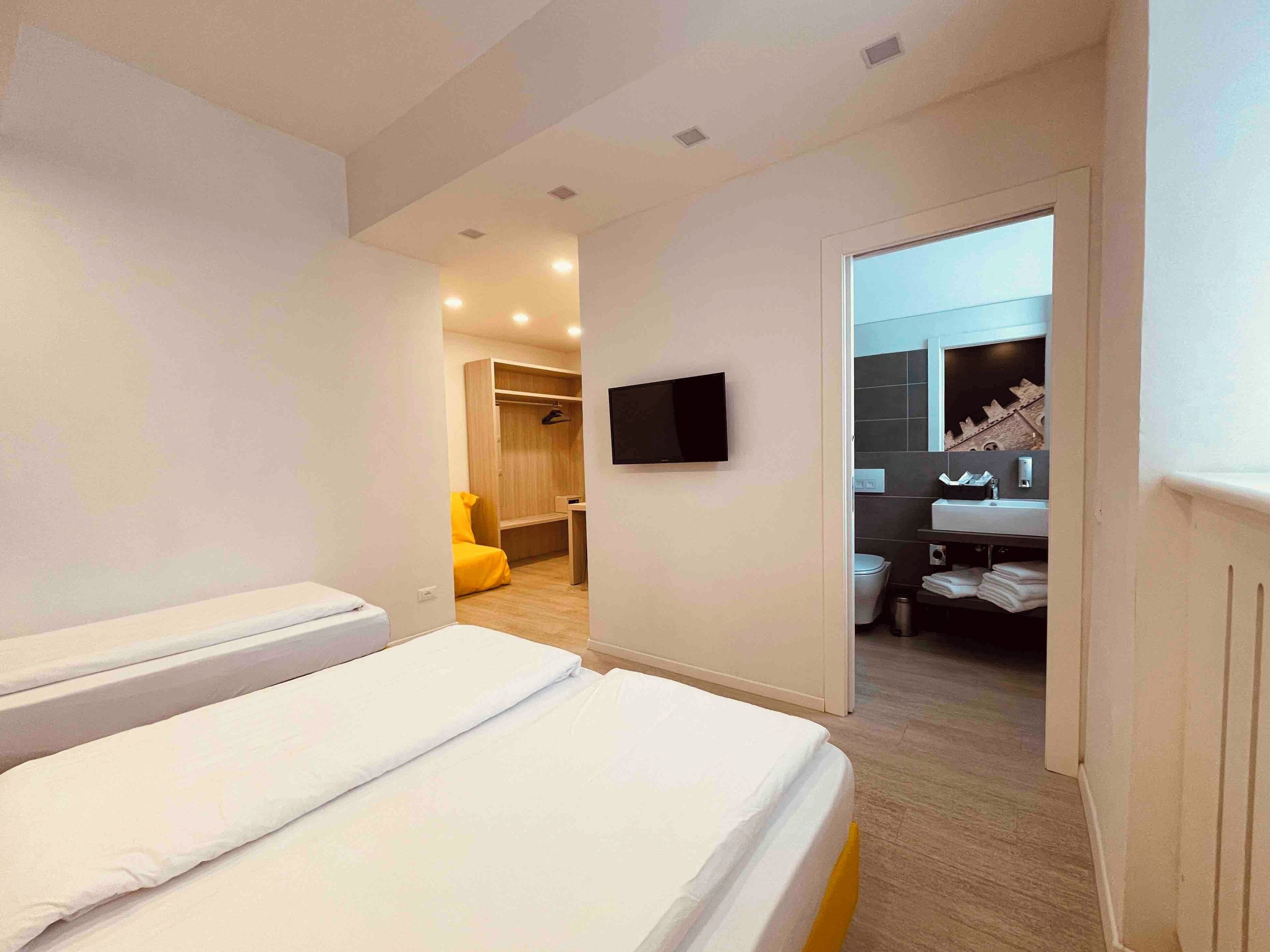 A modern hotel room with a large bed, a TV mounted on the wall, and a bathroom with a sink and mirror.