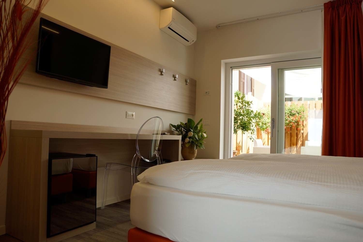 Une chambre d’hôtel équipée d’un lit, d’un bureau, d’une chaise, d’une télévision et d’une fenêtre donnant sur l’extérieur.