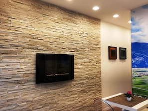 Una pared de piedra con un televisor montado, un cuadro enmarcado y una pintura de un paisaje.