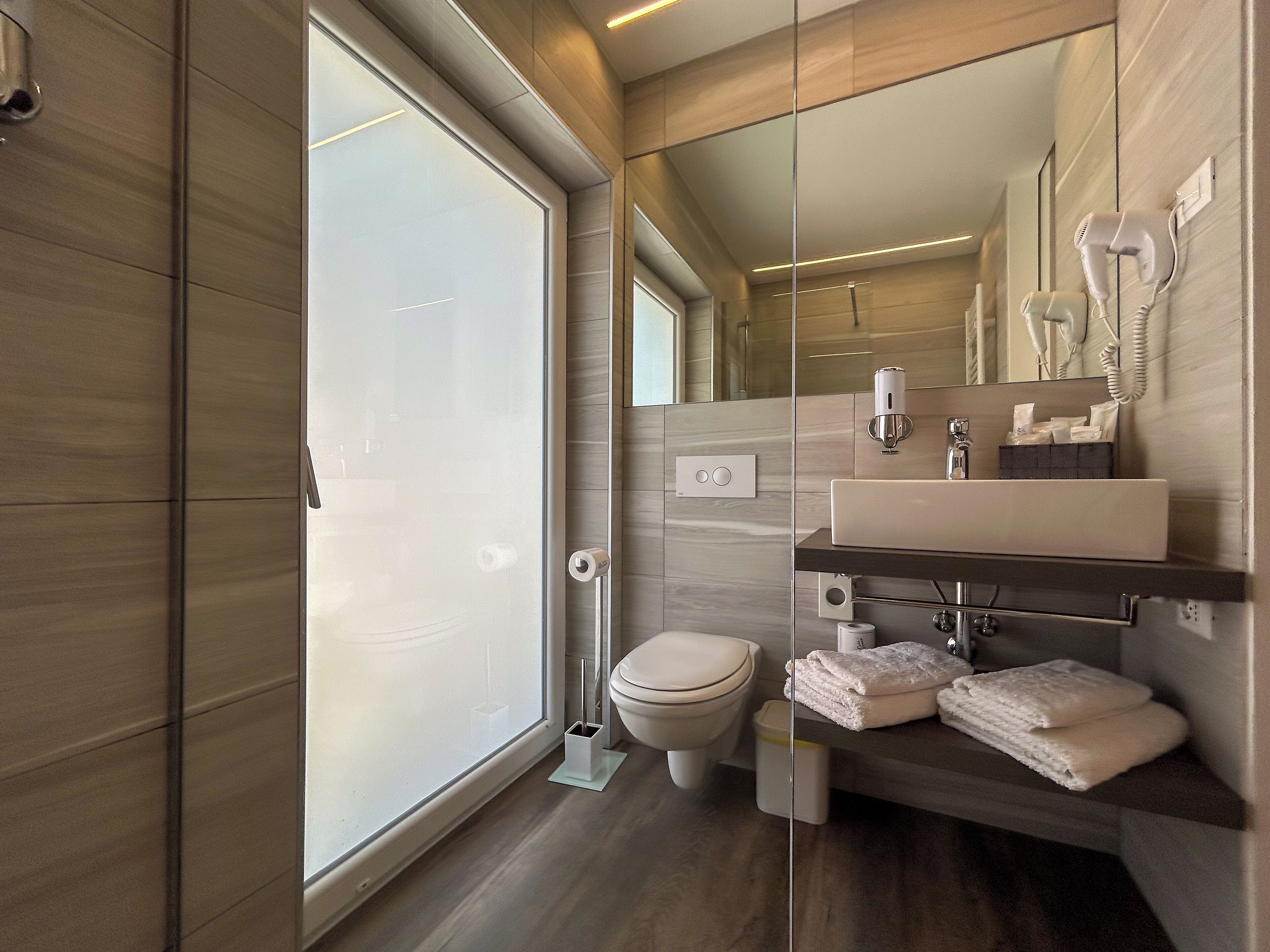 Un baño moderno con un espejo grande, un inodoro, un lavabo con toallero y una cabina de ducha de vidrio.