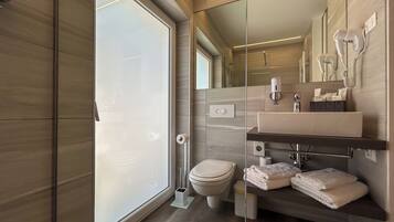 Un baño moderno con un espejo grande, un inodoro, un lavabo con toallero y una cabina de ducha de vidrio.