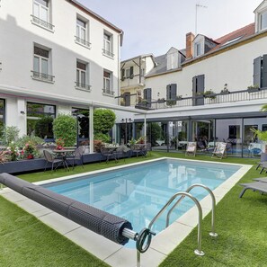 Una piscina moderna all'aperto con struttura in vetro, circondata da un prato curato e zone relax.