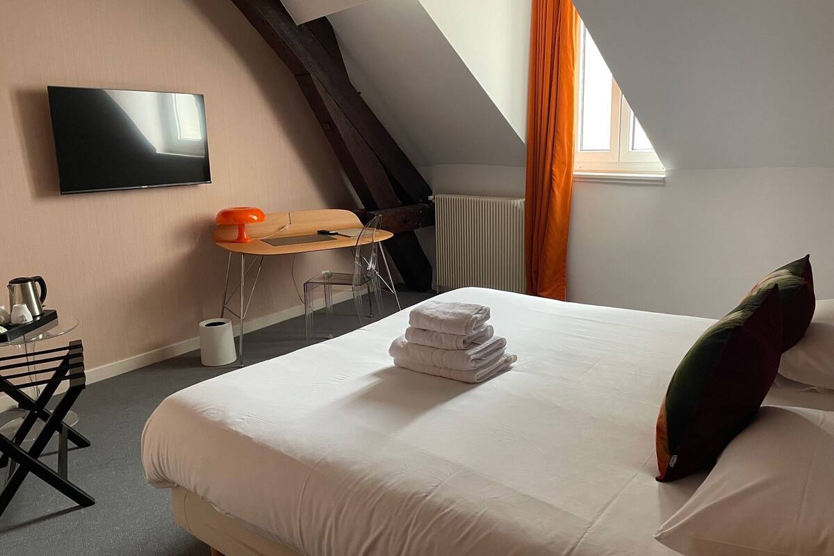 Hotelkamer met een bed, bureau, stoel, televisie en raam met gordijnen.