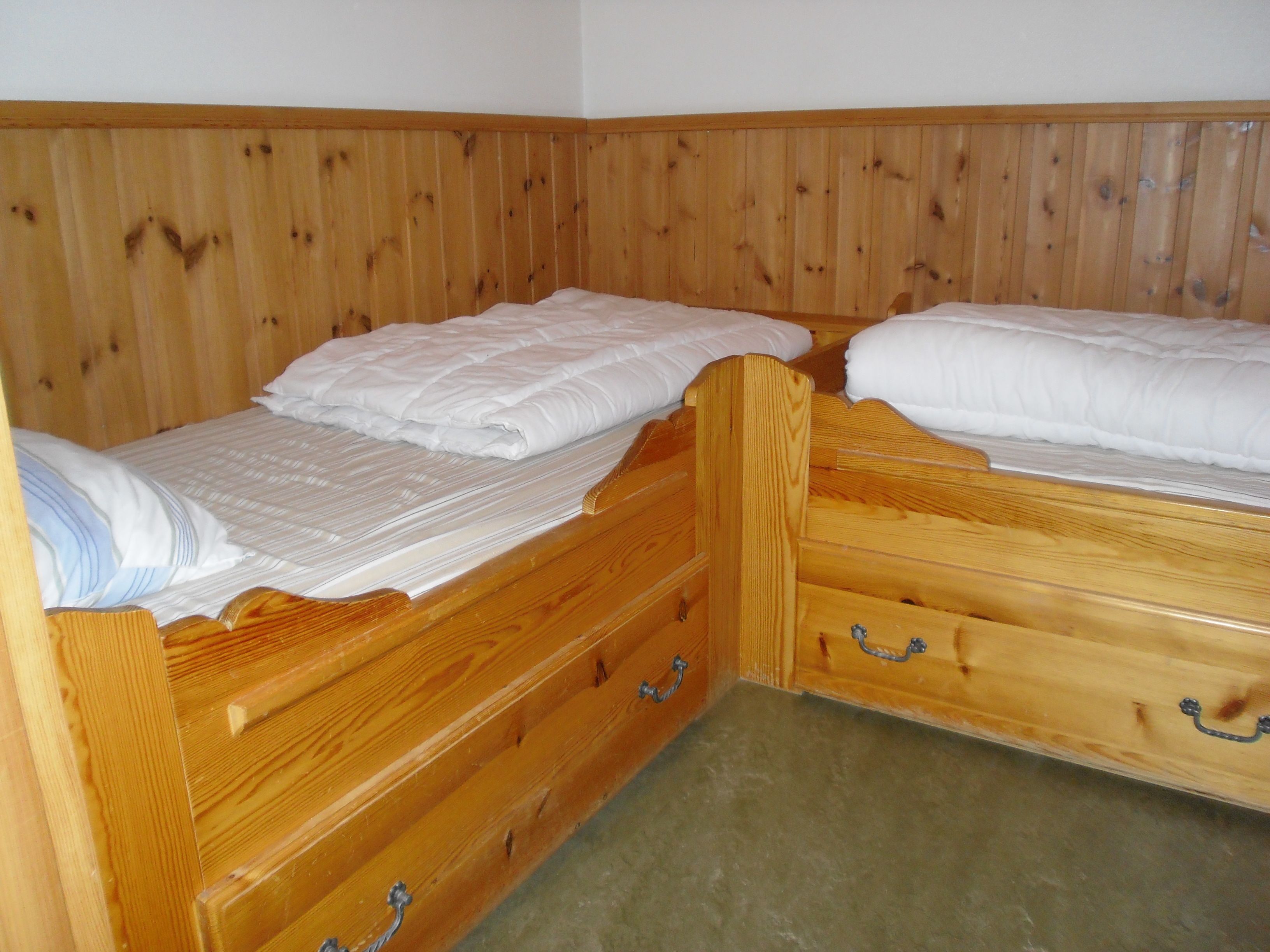 Un letto a castello in legno con due letti, ognuno con un materasso e dei cuscini bianchi. Ci sono delle maniglie metalliche sui cassetti.