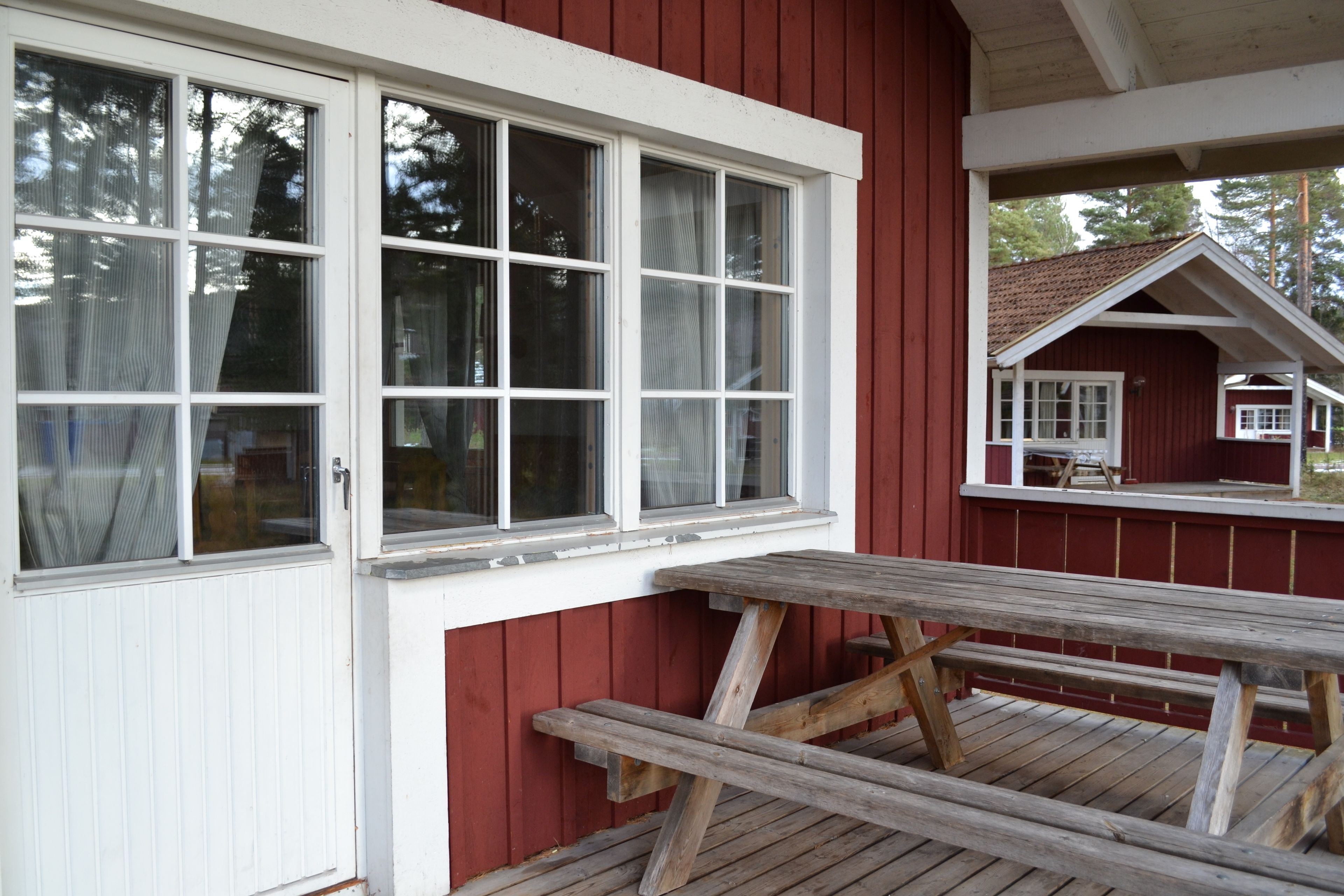 A wooden deck with a picnic table, a white door, and a red building with windows.