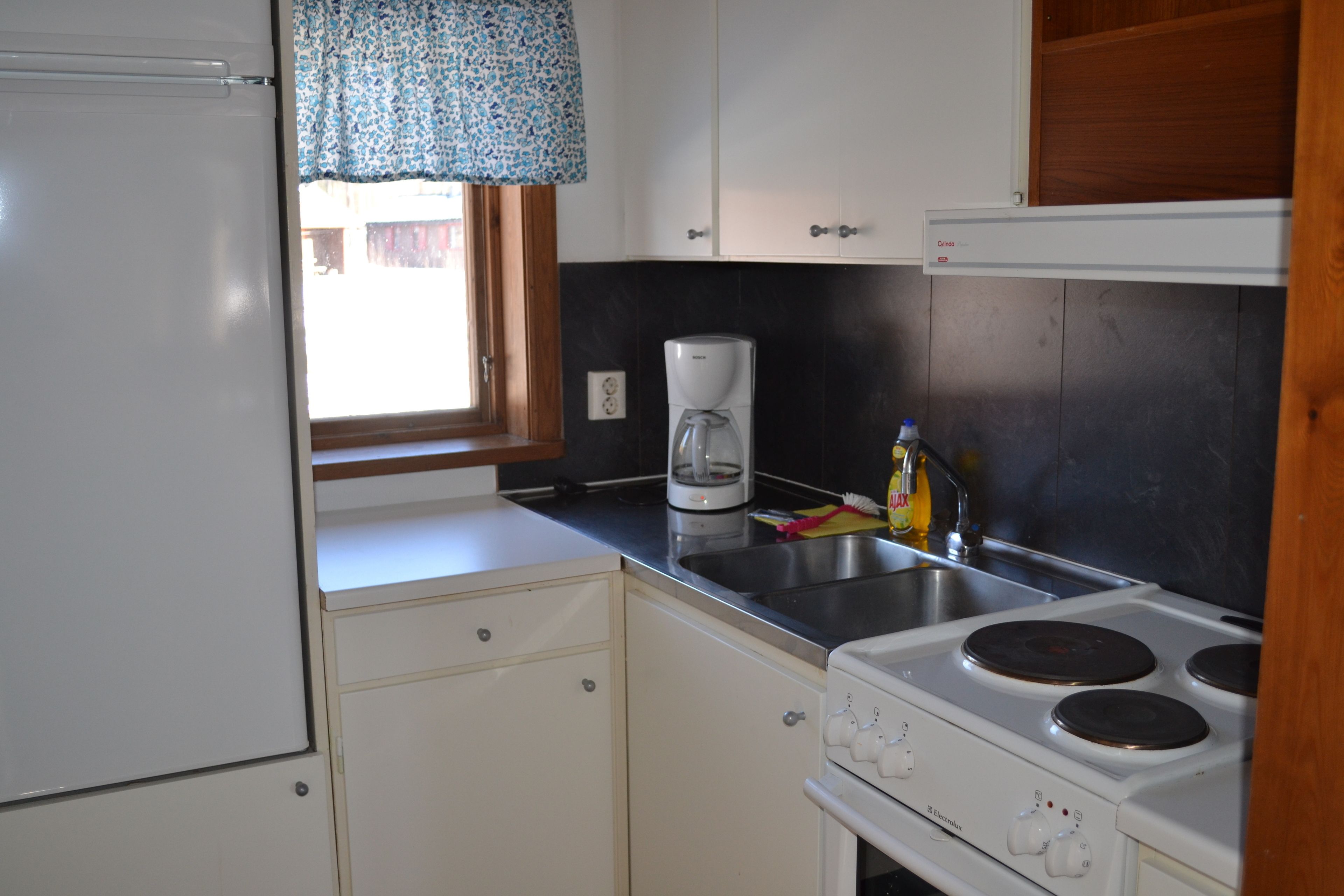 A compact kitchen with a refrigerator, a coffee maker, and a stove.