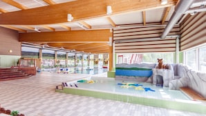 An indoor swimming pool with a wooden ceiling, a play area with colorful toys, and a view of a mountain landscape through large windows. - First Camp Enåbadet (Rattvik)