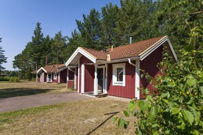 A row of red wooden cabins with pitched roofs, set in a wooded area.