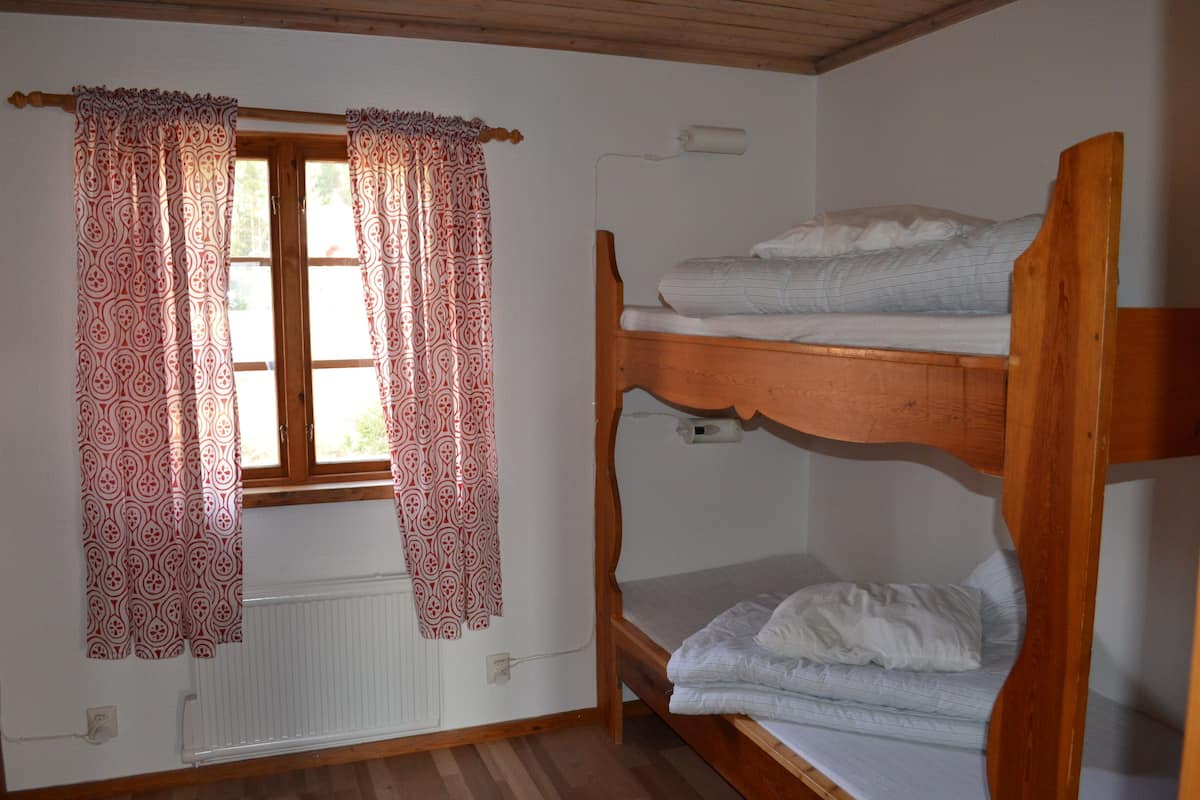 A room with a bunk bed, a window with patterned curtains, and a radiator.