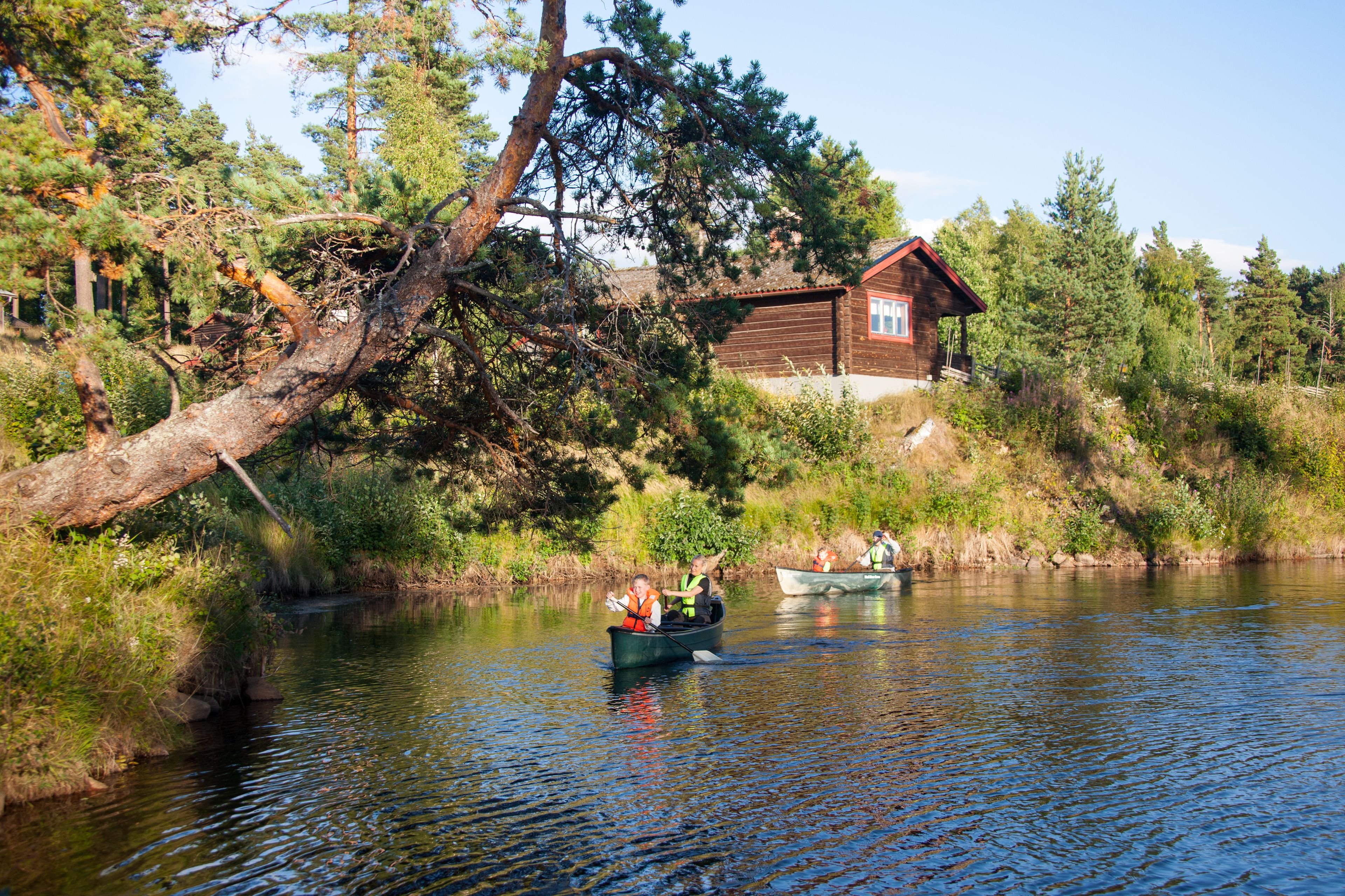 En stuga vid en flod, med en kanot i förgrunden och en annan i bakgrunden.