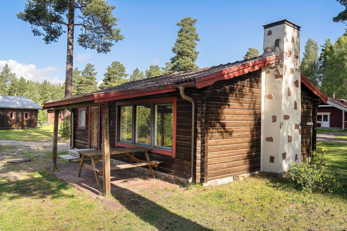 A rustic log cabin with a chimney, large windows, and a wooden deck.